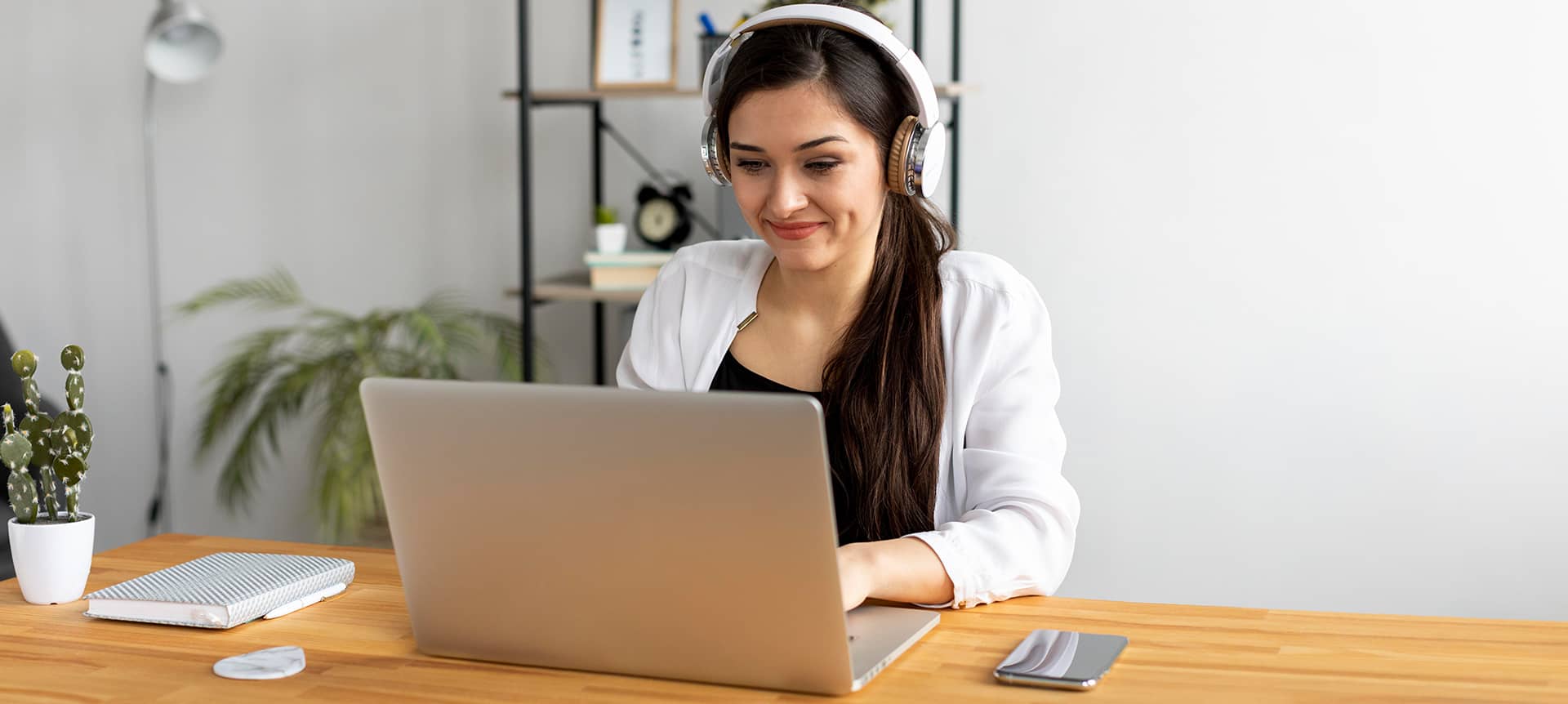 A female employee working on her laptop, smiling, and wearing headsets to hear a video assessment.